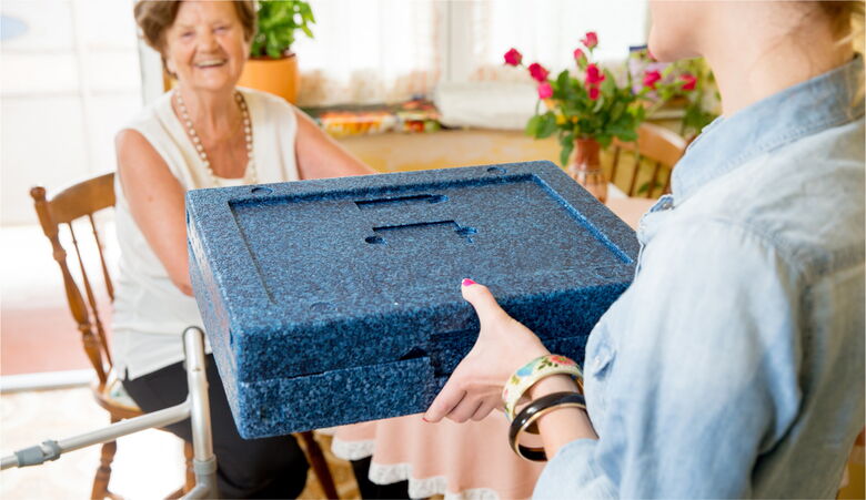 Übergabe einer Thermobox an eine lächelnde Seniorin – Der Menüservice „Essen auf Rädern“ von Reinery.