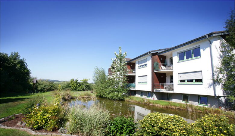 Außenansicht der modernen Wohnanlage in Appenhagen mit idyllischem Teich und weitläufiger Grünfläche.
