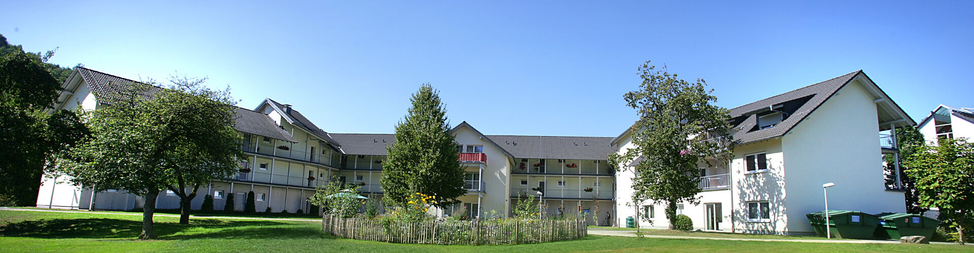 Außenansicht der weitläufigen, hellen Gebäudeanlage „Am Prinzen Heinrich“ in Morsbach, umgeben von Bäumen und Rasenflächen.