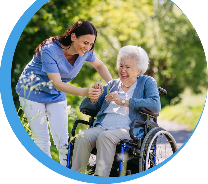 Eine Pflegekraft begleitet eine lachende Seniorin im Rollstuhl bei einem Ausflug im Grünen – herzliche Betreuung und Lebensqualität bei Reinery.