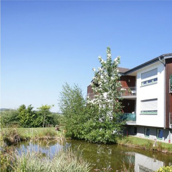 Außenansicht der Wohnanlage in Morsbach-Appenhagen mit idyllischem Teich und viel Grünfläche.